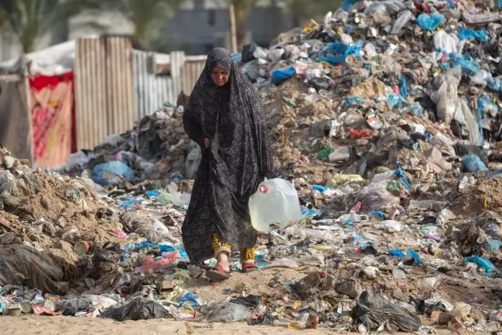 Una palestina lleva agua en una zona llena de basura cerca de Khan Yunis, en el sur de Gaza, en una imagen de archivo. EFE/HAITHAM IMAD